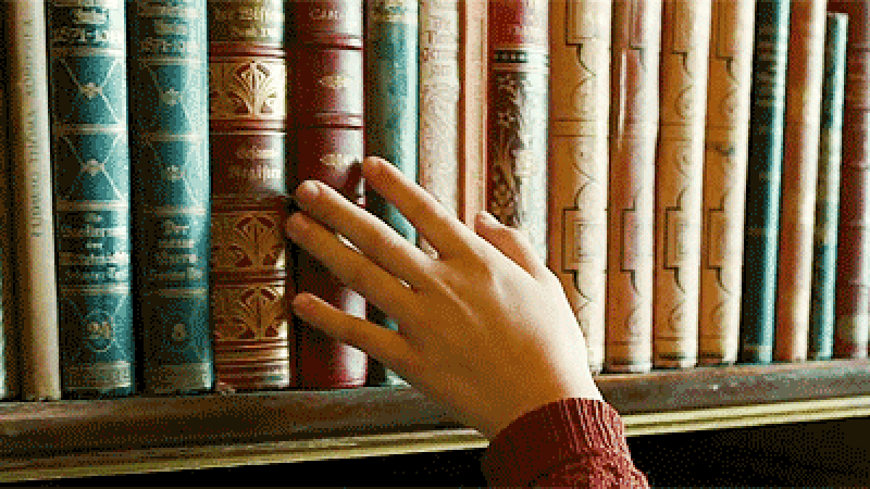 A hand moving along the spines of a shelf of books